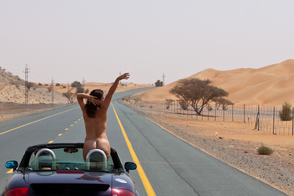 woman standing in car, middle of desert road