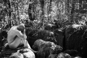 nude man sitting on mossy rock, black and white photo